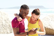 © mimagephotos - Happy young couple together at the beach using mobile phone