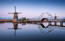 Spring Landscape With Beautiful Traditional Dutch Windmills Near The Water Channels With Drawbridge And Reflection In Water At Sunrise In Famous Kinderdijk, Netherlands