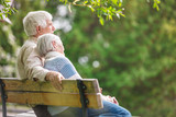 Fototapeta  - Elderly couple resting on a bench in the park