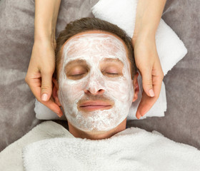 Face of man with cream mask and hands of beautician