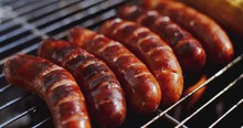 Six Tasty Juicy Sausages Grilling Over A Fire In A Portable Barbecue On A Summer Picnic  Close Up View Of The Grill
