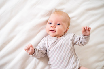 little baby boy lying on bed in onesie, white bedroom