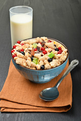 Wall Mural - full bowl of muesli with berries and spoon on a napkin near to the glass of milk on a dark wooden background