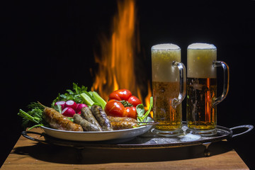 two beers and sausages with flame on background