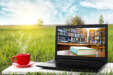 Laptop and cup of hot coffee on the background picturesque nature, outdoor office. E-book library concept with laptop computer and book. Old books on a wooden shelf. Travel concept. Business ideas.
