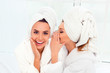 Girl in bathrobe and  towel on her head telling secret to her si