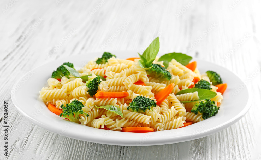 Boiled fusilli pasta with carrot, broccoli and basil on white plate