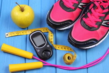 Glucometer, sport shoes, fresh apple and accessories for fitness on blue boards