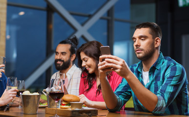 man with smartphone and friends at restaurant