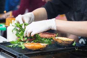 Wall Mural - Chef making beef burgers outdoor on open kitchen international food festival event. Street food ready to serve on a food stall.