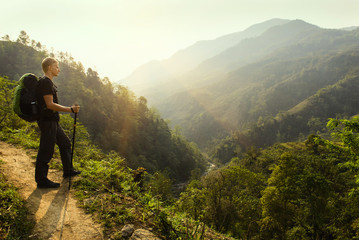 Man hiking with backpack holding trekking sticks in the mountain