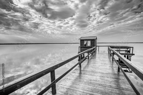 Fotografie, Obraz Old Wooden Pier For Fishing, Small House Shed And Beautiful Lake