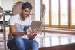 © GENETTICA - Young man smiling while using a tablet sitting on the stairs of