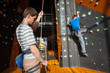 © anatoliy_gleb - Man stands on the ground near rock wall indoors and insuring the climber with rope and carbines