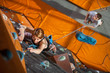 © anatoliy_gleb - Woman rock climbing with carbines and rope on an indoor rock-climbing wall. Man standing on the ground insuring the climber