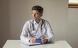 © GENETTICA - Frontal view of a young doctor looking to the side. He is sittin