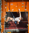 © anatoliy_gleb - Athletic man with special equipment and rope climbs on indoor wall, giving thumb up and smiling
