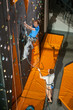 © anatoliy_gleb - Male climbing on an indoor rock-climbing wall, belayer standing on the ground belaying the climber