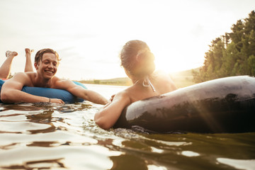 Wall Mural - Affectionate young couple floating on inner tubes in lake