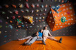© anatoliy_gleb - Two tired guys and one girl with closed eyes sitting on the orange mat near rock wall indoors. Bouldering