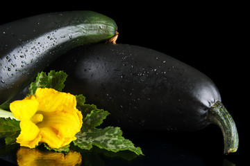 Cropped courgettes with flowers on black background