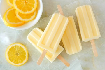 Poster - Lemon vanilla popsicles in a cluster with fresh lemon slices on a white marble background