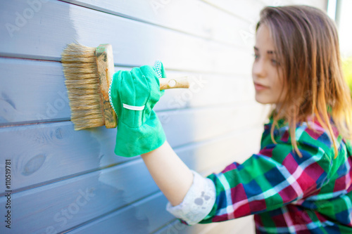 Fotografía Young woman applying protective varnish or paint on wooden house tongue and groove cladding elevation wall