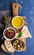 Mediterranean snacks set. Olives, oil, herbs and sliced ciabatta bread on yellow rustic oak board over painted dark blue background