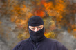Mann mit Sturmhaube vor einem Hintergrund aus Rauch und Flammen