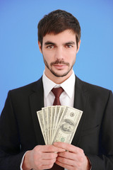 Poster - Attractive man in a suit holding fan of dollar banknotes on blue background