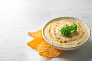 Wall Mural - Ceramic bowl of tasty hummus with chips and parsley on table