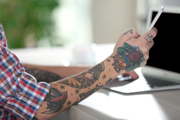 Wall Mural - Young man with tattoo using laptop and mobile phone at the table