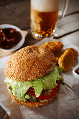 Wall Mural - Big tasty hamburger with snacks and glass mug of light beer on wooden table