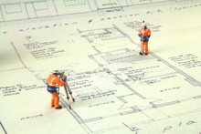 Two Miniature Figures In High-vis Uniform With A Theodolite Survey A House Blueprint