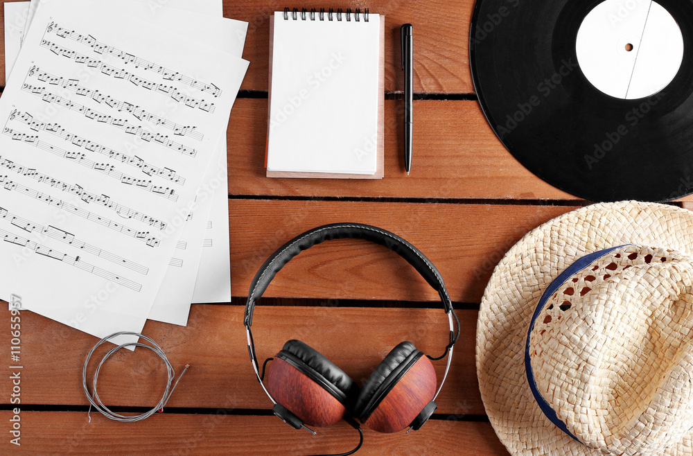 Headphones, music sheets and straw hat on wooden surface, top view