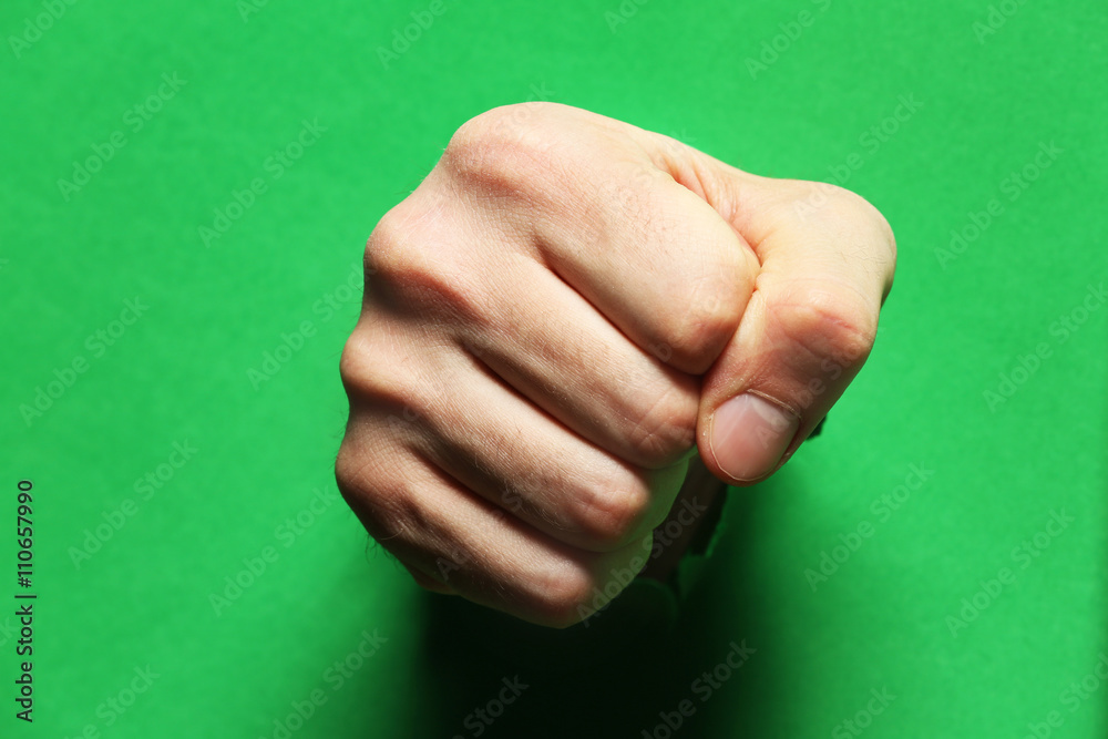 Male fist punching through green paper