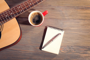 Wall Mural - Guitar with notebook and cup of coffee on wooden background