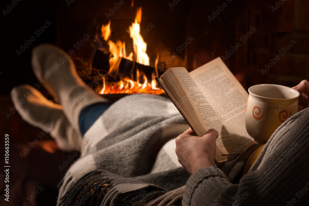 Woman reads book near fireplace - obrazy, fototapety, plakaty 