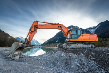 side view of orange shovel digger on gravel at lake and blue sky