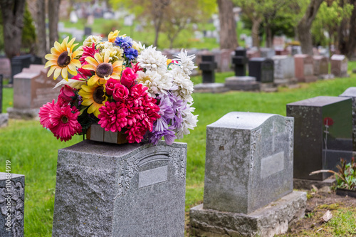 Cuadros en Lienzo Flowers on a tombstone in a cemetary with headstones in the background
