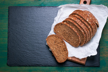 Wall Mural - Cut in slices loaf of bread on a cut board on a green vintage wooden background with place for text, horizontal, top view