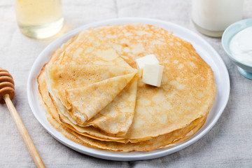 Wall Mural - Thin crepes or pancakes with butter, honey and sour cream on a rustic textile background