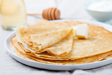 Wall Mural - Thin crepes or pancakes with butter, honey and sour cream on a rustic textile background
