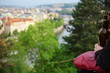 Young person enjoys good weather, drinks beer and observes the panoramic aerial view of the city of Prague.
