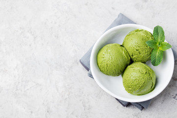 Green tea matcha ice cream scoop in white bowl on a grey stone background. Copy space Top view