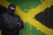 Dangerous Man In A Mask Standing Near A Wall With Painted National Flag Of Jamaica