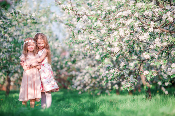 adorable little girls in blooming cherry tree garden on spring day