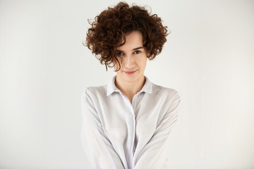 Headshot of young attractive hipster woman with dark curly hair looking at the camera with happy and confident expression. Poatrait of trendy student girl having fun before classes at university