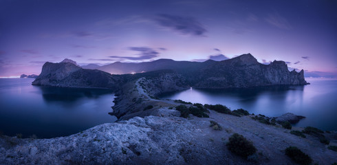 Wall Mural - Night landscape with mountains, sea, starry sky and city lights. Amazing view with rocks at dusk in Crimea