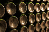 Fototapeta  - Dusty old wine bottles stacked in the wine cellar